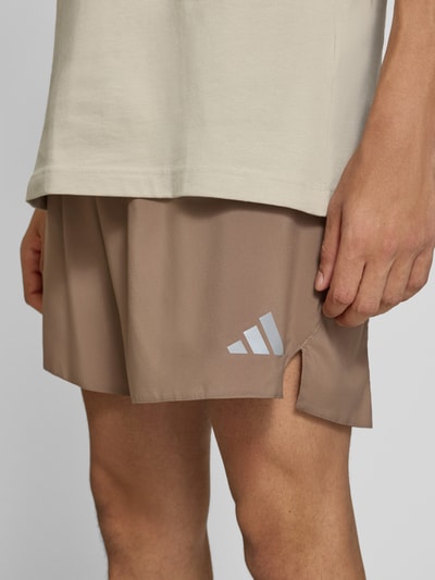 Männermodel trägt Regular Fit Sportshorts mit Logo-Print Modell 'Run Ess Shor M' von adidas, beige Farbe, glatte Struktur, Nahaufnahme Oberschenkel, Herren Sportshorts von adidas Training.