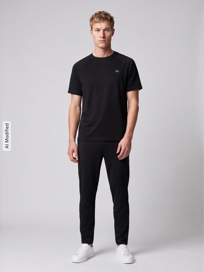 Mężczyznamodel nosi Slim Fit Trainingshose mit Logo-Patch von Lacoste Sport, czarne, gładka tekstura, pełny widok z przodu, KI-modifiziertes Bild