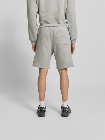 Männermodel trägt Sweatshorts aus Baumwoll-Mix von RHUDE in Grau, Eingrifftaschen, Label-Stitching, Gerade Passform, Ganzkörperansicht Rückansicht.