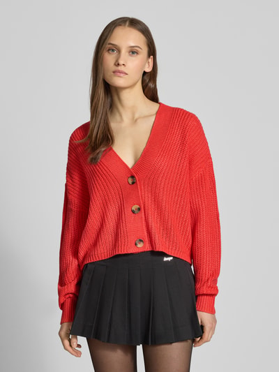 Frauenmodel trägt Regular Fit Strickjacke mit einreihiger Knopfleiste Modell 'CAROL NICE' von ONLY, Optik: Unifarben, Strickoptik, Cropped-Länge, Label-Stitching-Applikation, tiefer V-Ausschnitt, Langarm, gerippter Rumpf- und Ärmelabschluss, Materialverarbeitung: Strick, Ganzkörperansicht von vorne.