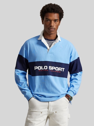 Männermodel trägt Regular Fit Poloshirt aus reiner Baumwolle von Polo Ralph Lauren in Hellblau, Dunkelblau, mit Label-Schriftzug, Ganzkörperansicht von vorne.