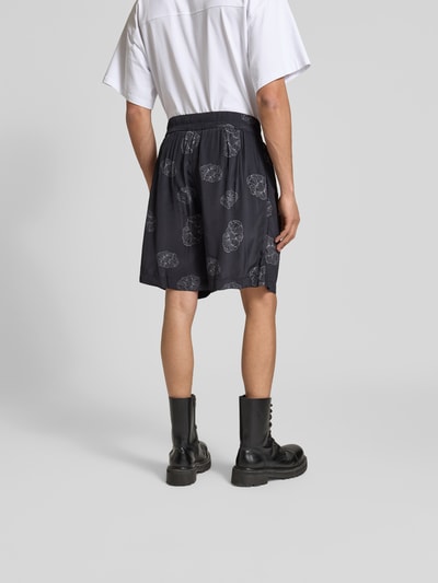 Männermodel trägt Shorts aus reiner Viskose von Officine Générale in Schwarz mit weißem Muster, Relaxed Fit, Ganzkörperansicht Rückansicht.