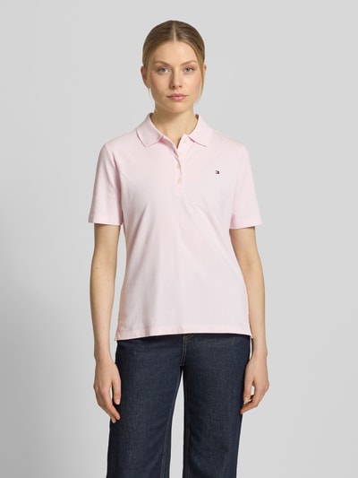 Vrouwenmodel draagt Regular Fit Poloshirts aus Baumwoll-Mix van Tommy Hilfiger in effen lichtroze piqué katoenmix, korte knoopsluiting, korte mouw, logo-stitching op de borst, polokraag, V-hals, regular fit, voorkant volledig zichtbaar, totale lichaamsaanzicht.