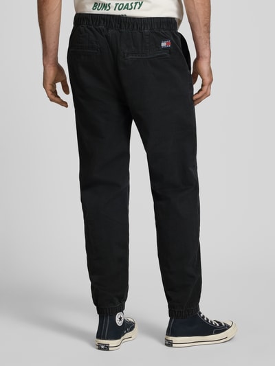 Männermodel trägt Straight Fit Jeans aus reiner Baumwolle von Tommy Jeans in schwarzer Denim-Optik mit elastischem Bund, Ganzkörperansicht Rückansicht.