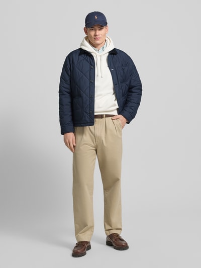 Männermodel trägt Regular Fit Steppjacke mit Kentkragen von Polo Ralph Lauren in Dunkelblau, sichtbare Knopfleiste, Brusttasche, Eingrifftaschen, Label-Stitching, Kombi aus Beige und Blau, Rückenlänge 70 cm, Schulterbreite 51 cm, Brustweite 58 cm, Ärmellänge 67 cm, Ganzkörperansicht von vorne.
