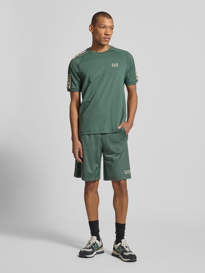 Männermodel trägt T-Shirt aus Viskose-Mix mit Logo von EA7 Emporio Armani in Grün mit Rundhalsausschnitt, Regular-Fit, Ganzkörperansicht von vorne.