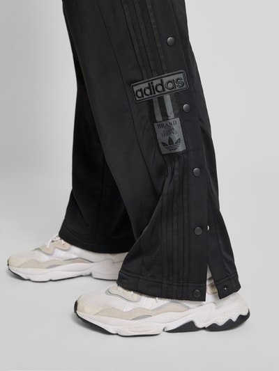 Männermodel trägt Sweatpants mit elastischem Bund von adidas Originals in Schwarz mit Label-Detail und Eingrifftaschen, Nahaufnahme Beinpartie.