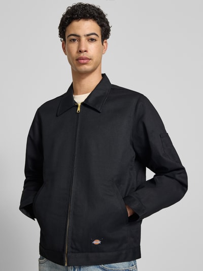 Männermodel trägt Jacke mit Reißverschluss Modell 'UNLINED EISENHOWER' von Dickies aus schwarzem Material-Mix, Regular-Fit, Eingrifftaschen, Label-Detail, Ganzkörperansicht von vorne, Rückenlänge 67 cm, Schulterbreite 39 cm, Brustweite 53 cm, Ärmellänge 66 cm, Größe M.