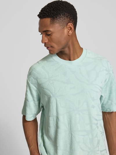Männermodel trägt Regular Fit T-Shirt aus Baumwoll-Mix Modell 'TE_FLOWER' von BOSS Orange in Mintgrün mit floraler Struktur, Nahaufnahme Oberkörper.