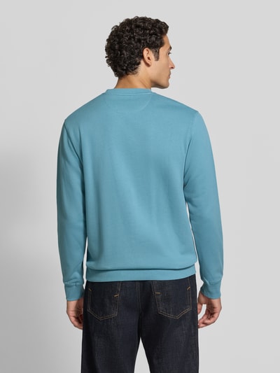 Männermodel trägt Sweatshirt mit Label-Patch von Scotch & Soda in Hellblau, reine Baumwolle, lockerer Schnitt, Ganzkörperansicht Rückansicht.