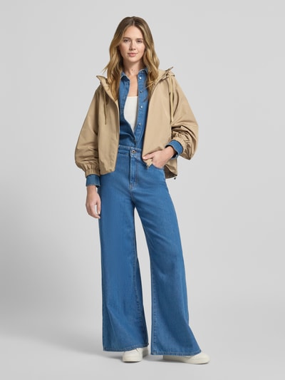 Frauenmodel trägt Relaxed Fit Regenjacke mit Baumwoll-Anteil Modell 'ROMANA' von Weekend Max Mara in Beige, unifarben, Kapuze, wasserabweisend, Logo-Patch, elastische Ärmel, seitliche Eingrifftaschen, Ganzkörperansicht von vorne.