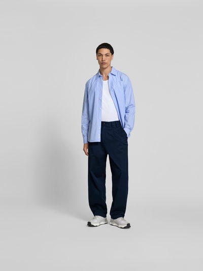 Männermodel trägt Wide Fit Stoffhose mit Bundfalten von Forét in Dunkelblau, Baumwoll-Mix, Seitentaschen, Ganzkörperansicht von vorne.