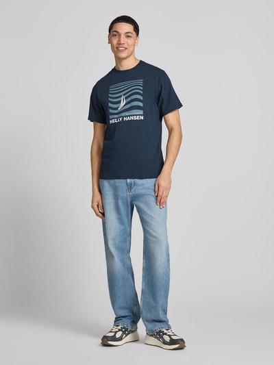 Männermodel trägt T-Shirt mit Logo- und Motiv-Print Modell 'SHORELINE' von Helly Hansen, Reine Baumwolle, Gerader-Schnitt, Ganzkörperansicht von vorne.