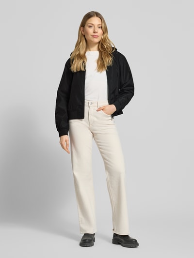 Frauenmodel trägt Regular Fit Blouson mit Kapuze von Tom Tailor Denim, Optik: Unifarben, Passform: Regular-Fit, Verschluss: Reißverschluss, Kragenform: Kapuze, Ärmelform: Langarm, Ärmelabschluss: Gerippt, Rumpfabschluss: Gerippt, Funktion: wasserabweisend, Wasserdicht, Atmungsaktiv, mit seitlichen Eingrifftaschen, schwarze glatte Textur, Ganzkörperansicht von vorne.