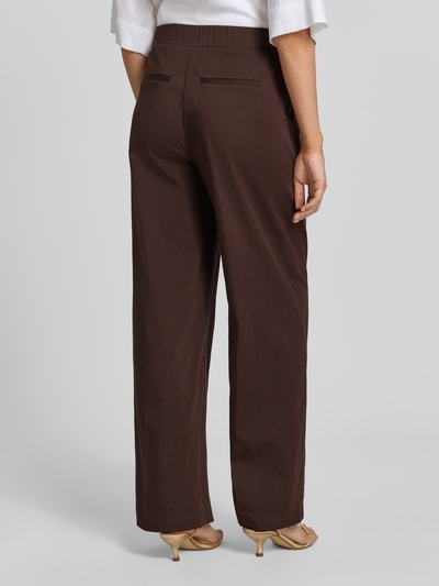 Männermodel trägt spodnie materiałowe z mieszanki bawełny z dodatkiem streczu, krój loose fit, francuskie wpuszczane kieszenie, model 'Mucia Base' od OPUS PANTS, kolor brązowy, elastyczny pas, tył kieszenie z wypustką, długość wewnętrzna nogawki 80 cm w rozmiarze 36, szerokość w rozmiarze 36: 31 cm, zdjęcie całej sylwetki z tyłu.
