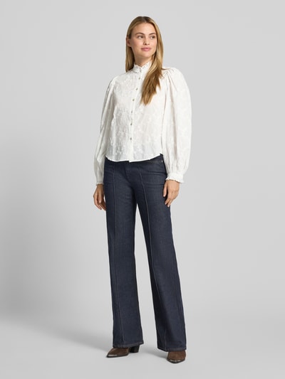 Frauenmodel trägt Bluse aus reiner Baumwolle mit Stehkragen Modell 'ROMA' von MANGO, weiße Stickerei, ballonartige Ärmel, gerade Passform, Ganzkörperansicht von vorne.