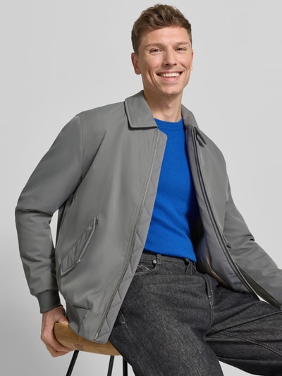 Männermodel trägt Jacke mit Reißverschluss von MCNEAL in Grau mit Kentkragen, Pattentaschen, gerippte Abschlüsse, Regular-Fit, Ganzkörperansicht von vorne. Rückenlänge 68 cm, Schulterbreite 48 cm, Brustweite 57 cm, Ärmellänge 65 cm bei Größe M.