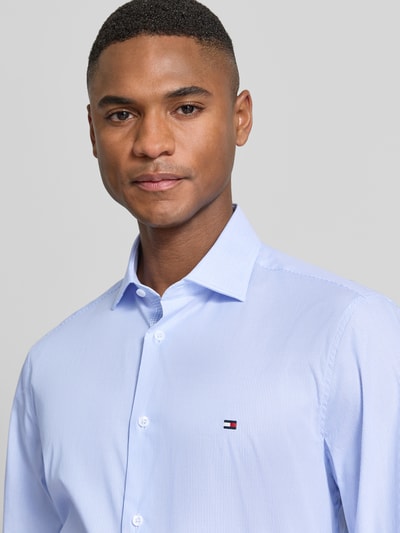 Männermodel trägt Slim Fit Businesshemd aus Baumwoll-Mix von Tommy Hilfiger, efekt: wzór w paski, kołnierzyk typu kent, długa listwa guzikowa, wyhaftowane logo, długi rękaw, mankiet zapinany na 1 guzik, mieszanka bawełny, krój slim fit, kolor jasnoniebieski, struktura gładka, nahaufnahme górnej części ciała.