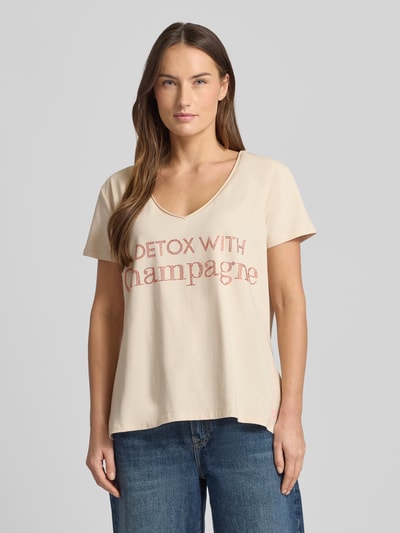 Frauenmodel trägt Loose Fit T-Shirt mit V-Ausschnitt von miss goodlife, beigefarbener Baumwoll-Elasthan-Mix, Statement-Print, Nahaufnahme Oberkörper.
