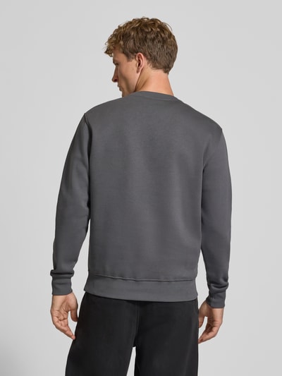 Männermodel trägt Sweatshirt mit Label-Details von Alpha Industries in Dunkelgrau, gerader Schnitt, Rückenansicht, Ganzkörperansicht Rückansicht. Baumwoll-Mix, gerippte Abschlüsse, Größe M: Rückenlänge 69 cm, Ärmellänge 72 cm.
