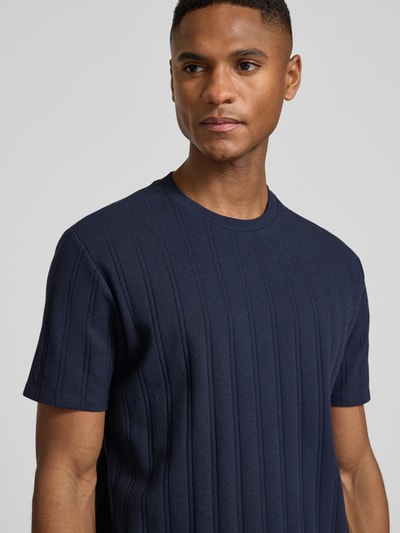 Męski model nosi Regular Fit T-Shirt aus Baumwolle od Guess, bawełna, krój regular fit, okrągły dekolt, detal z logo, długość tyłu 69 cm w rozmiarze M, zbliżenie na górną część ciała