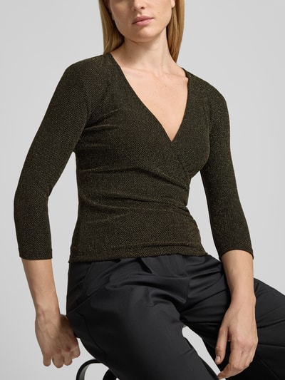 Kobiece modelka nosi Schimmerndes Blusenshirt mit V-Ausschnitt von Christian Berg Woman, Mieszanka materiałów z dodatkiem streczu, krój slim fit, efekt błyszczący, dekolt w serek, długość tyłu w rozmiarze S: 55 cm, długość rękawów w rozmiarze S: 47 cm, czarne spodnie, proste tło, kolor głęboki czarny ze złotymi detalami, tekstura gładka, nahaufnahme górnej części ciała.