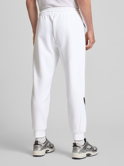 Männermodel trägt Sweatpants mit elastischem Bund von adidas Sportswear in Weiß, lockerer Schnitt, Reißverschlusstaschen, Ganzkörperansicht Rückansicht.