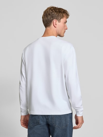 Männermodel trägt weißes Relaxed Fit Langarmshirt aus Baumwoll-Mix Modell 'SCASPIAN' von ONLY & SONS, blaue Jeans, Ganzkörperansicht Rückansicht.