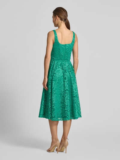 Frauenmodel trägt Knielanges Kleid mit Allover-Spitzen-Besatz von Rinascimento in Grün, taillierte und ausgestellte Passform, ärmellos, abnehmbarer Gürtel, elastischer Material-Mix, strukturierte Spitzen-Textur, Ganzkörperansicht Rückansicht.
