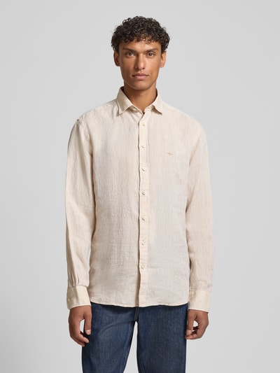 Męski model nosi Slim Fit Leinenhemd mit Haifischkragen von Fynch-Hatton w kolorze beżowym, wyhaftowane logo, krój slim fit, czysty len, długość tyłu w rozmiarze M: 77 cm, szerokość ramion w rozmiarze M: 47 cm, długość rękawów w rozmiarze M: 61 cm, widok całej sylwetki z przodu.