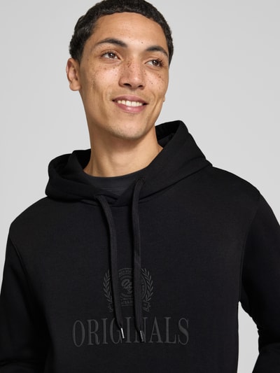 Männermodel trägt Hoodie aus Baumwoll-Mix Modell 'FREDERIKS' von JACK & JONES mit Kapuze, Label-Print, Nahaufnahme Oberkörper.