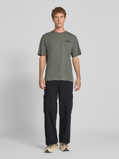 Männermodel trägt Oversized T-Shirt aus reiner Baumwolle Modell 'PEANUTS' von ONLY, Heren T-Shirt, olijfgroen, zwart cargobroek, Ganzkörperansicht von vorne