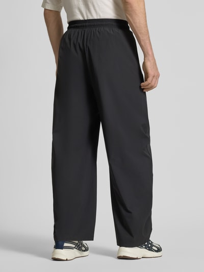 Männermodel trägt Oversized Jogpants mit Reißverschlusstaschen von adidas Sportswear in Schwarz, Elastischer-Material-Mix, Ganzkörperansicht Rückansicht.