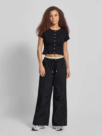 Frauenmodel trägt Regular Fit Trackpants mit Kontraststreifen von Tommy Jeans, efekt: jednolity kolor, krój regular fit, aplikacja: paski w kontrastowym kolorze, pas z logo, zapięcie: tunel, ściągacz: elastyczny, dwie warstwy pasa, kieszenie zapinane na zamek błyskawiczny po bokach, kieszeń z tyłu, Ganzkörperansicht von vorne