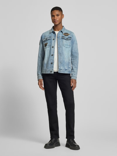 Męski model nosi Jeansjacke mit Label-Patches und Brusttaschen od PME Legend, niebieski denim, prosty krój, widok całej sylwetki z przodu. Szerokość w rozmiarze M: 53 cm, długość tyłu: 65 cm, szerokość ramion: 44 cm, długość rękawa: 67 cm.