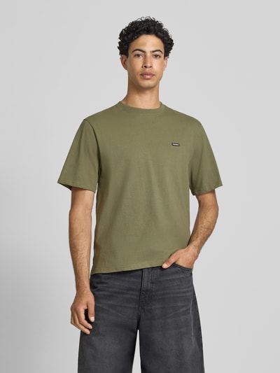 Männermodel trägt T-Shirt mit Label-Patch und Rundhalsausschnitt von REVIEW, reine Baumwolle, Boxy Fit, olive, Ganzkörperansicht von vorne