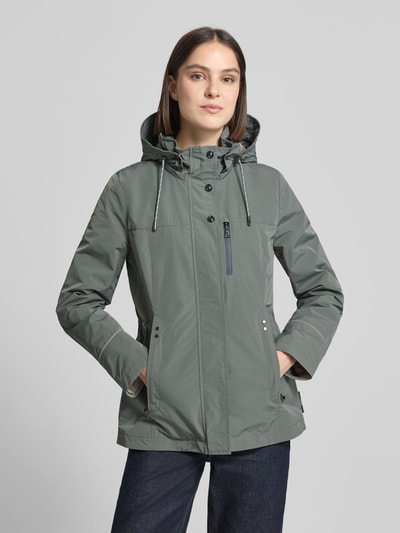 Frauenmodel trägt Funktionsjacke mit Brusttasche von Gil Bret in Grau mit Kapuze, Stehkragen und Tunnelzug, Nahaufnahme Oberkörper. Taillierte Passform, Brustweite 47 cm, Schulterbreite 41 cm, Rückenlänge 74 cm, Ärmellänge 65 cm bei Größe 36.