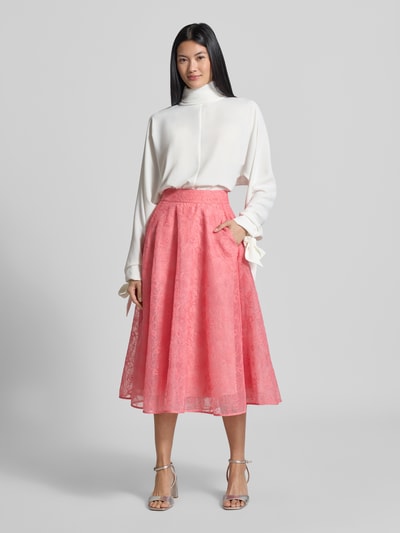 Frauenmodel trägt Relaxed Fit Langarmbluse mit Rollkragen von Emporio Armani in Weiß, langärmliges Design mit Zierschleifen am Ärmelabschluss, kombiniert mit rosa weitem Rock, Ganzkörperansicht von vorne.