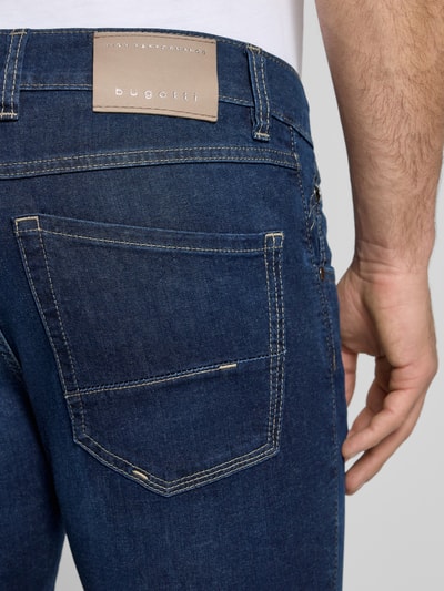 Mężczyzna nosi Regular Fit Jeans mit Eingrifftaschen od bugatti, bawełniany materiał z domieszką stretchu, niebieski denim, widoczne szwy, detal tyłu, szerokość w rozmiarze 32/32: 44 cm, długość nogawki wewnętrznej w rozmiarze 32/32: 80 cm, ujęcie z tyłu zbliżenie na kieszeń
