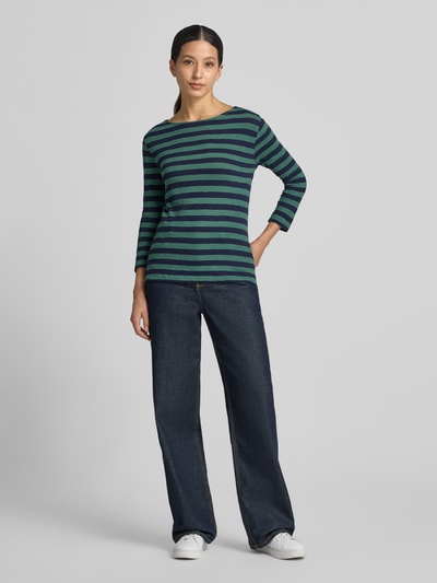 Frauenmodel trägt Longsleeve mit 3/4-Arm von Christian Berg Woman aus reiner Baumwolle, gerader Schnitt, Rundhalsausschnitt, grün-blau gestreift, kombiniert mit weiter Jeans und weißen Sneakern, Ganzkörperansicht von vorne.