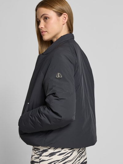 Modelka nosi Bomberjacke mit Daunen-Feder-Füllung von Moose Knuckles, czarna, prosta sylwetka, elastyczny materiał, kaptur z tunelem, zamek dwukierunkowy, szerokość w rozmiarze S: 60 cm, długość tyłu: 60 cm, długość rękawa: 55 cm, tekstura matowa, widoczne przeszycia, detal logo na rękawie, całkowity widok z przodu