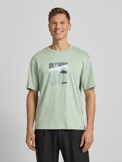 Männermodel trägt Relaxed Fit T-Shirt aus reiner Baumwolle Modell 'JOIN' von BOSS Green in Hellgrün mit Motiv-Print, Ganzkörperansicht von vorne.