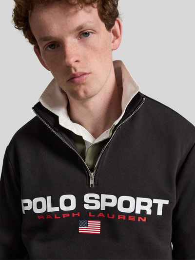 Männermodel trägt Relaxed Fit Troyer aus Baumwoll-Mix von Polo Ralph Lauren in Schwarz mit weiß-rotem Logo-Print, Nahaufnahme Oberkörper. Herren Troyer von Polo Ralph Lauren.