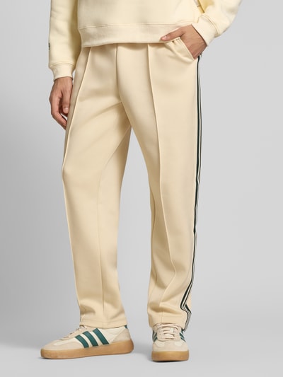Männermodel trägt Regular Fit Sweatpants mit elastischem Bund Modell 'RIBER' von Only & Sons, cremefarben, Kontraststreifen, Nahaufnahme Unterkörper.