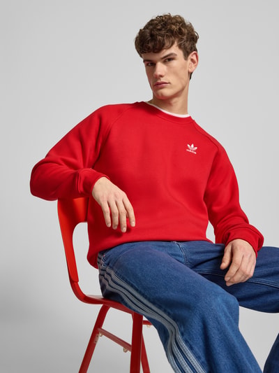 Männermodel trägt Sweatshirt mit Logo und Rundhalsausschnitt von adidas Originals in Rot, Baumwoll-Elasthan-Mix, Regular Fit, Nahaufnahme Oberkörper.