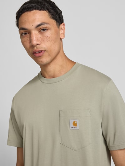 Männermodel trägt Regular Fit T-Shirt mit Brusttasche von Carhartt Work In Progress in Beige, Reine Baumwolle, Rundhalsausschnitt, Label-Patch, Nahaufnahme Oberkörper. Rückenlänge bei Größe M: 71 cm.