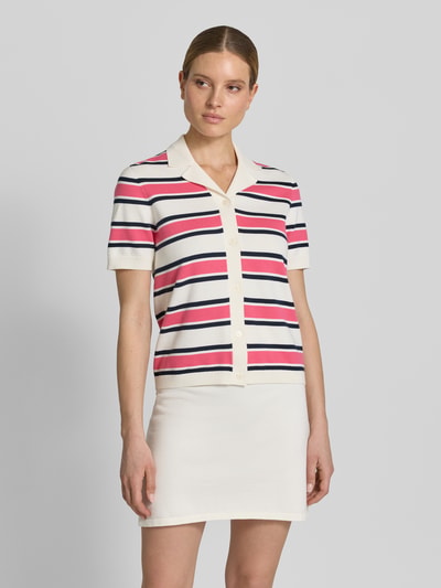 Frauenmodel trägt Regular Fit Poloshirt aus reiner Bio-Baumwolle Modell 'AMOUR' von Selected Femme, gestreift in Weiß, Pink und Dunkelblau, kurzarm, Stricktextur, Knopfleiste, Polokragen, Ganzkörperansicht von vorne.