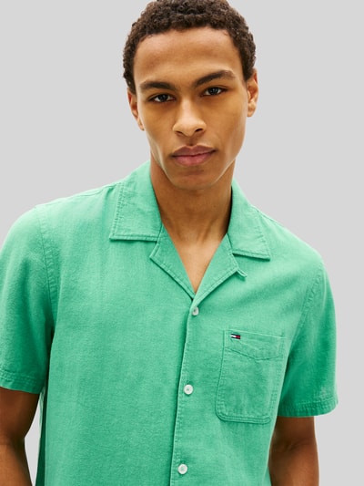 Männermodel trägt Regular Fit Freizeithemd aus Leinen-Baumwoll-Mix von Tommy Jeans in Optik: Unifarben, Nahaufnahme Oberkörper. Materialverarbeitung: Flammgarn, Kentkragen, durchgehend Knopfleiste, Kurzarm, Logo-Stitching auf Brusttasche.