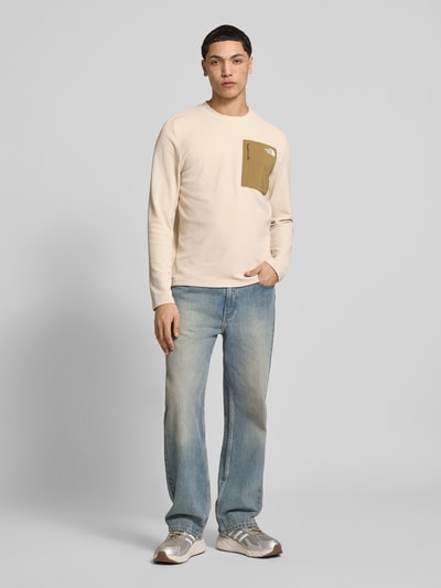 Męski model nosi bluzkę z długim rękawem z elastycznej mieszanki materiałów model 'KECHA' od The North Face, prosty krój, okrągły dekolt, Napoleontasche, detal z logo, długość tyłu w rozmiarze M: 67 cm, jasne kolory, całkowity widok z przodu.