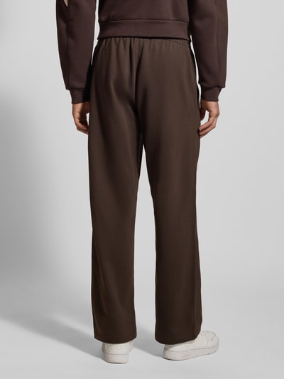 Männermodel draagt Straight Fit Sweatpants met logostitching van adidas Originals in donkerbruin, puur katoen, elastische band, binnenbeenlengte maat M 78 cm, ganzekörperaanzicht achteraan.